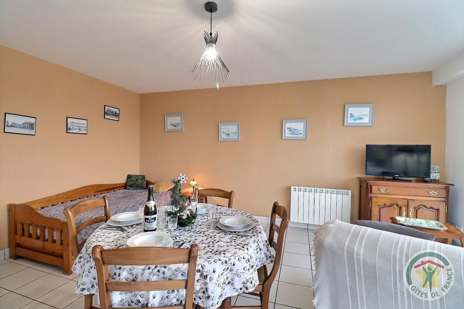 Ein Essbereich mit einem runden Tisch, Stühlen, einer Chandelüstere, einem Fernseher und gerahmten Bildern an der Wand.