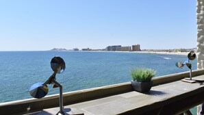 Een balkon met uitzicht op zee, een plant in pot en twee windgongjes.