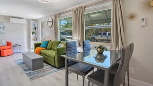 A modern living room with a glass dining table, green and orange sofas, and a large window with curtains. - Turtle Walk - Walk to Gorgeous Beach! WALK to 12 different Restaurants! (Longboat Key)