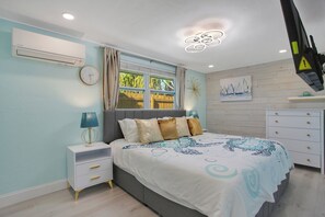 A bedroom with a bed, bedside tables, a window, and a wall-mounted air conditioner. - Turtle Walk - Walk to Gorgeous Beach! WALK to 12 different Restaurants! (Longboat Key)