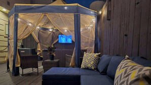 A cozy outdoor seating area with a canopy, a sofa, and a television screen. - Galleria Ashford Retreat | Jacuzzi | Sleeps 9 (Houston)