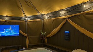 A hot tub with a television screen, a potted plant, and towels on a wooden bench. - Galleria Ashford Retreat | Jacuzzi | Sleeps 9 (Houston)