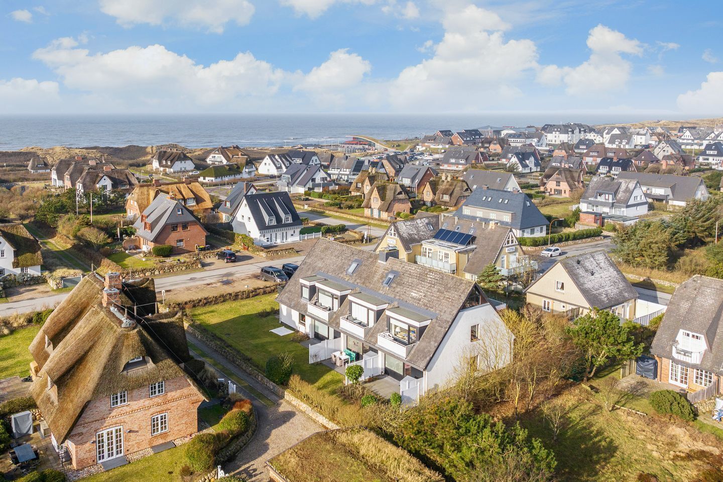 A coastal village with traditional and modern houses, a clear view of the sea, and a well-maintained grassy area.