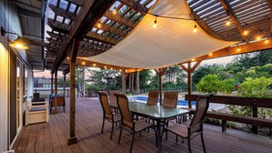A wooden deck with a glass-top table and chairs, surrounded by a pergola with string lights. - Russian River Wine Country Retreat Near Healdsburg: Pool, AC & EV Charger (Forestville)