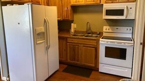 Une cuisine de taille réduite, dotée de meubles en bois, d’un réfrigérateur blanc, d’un four à micro-ondes et d’une cuisinière.