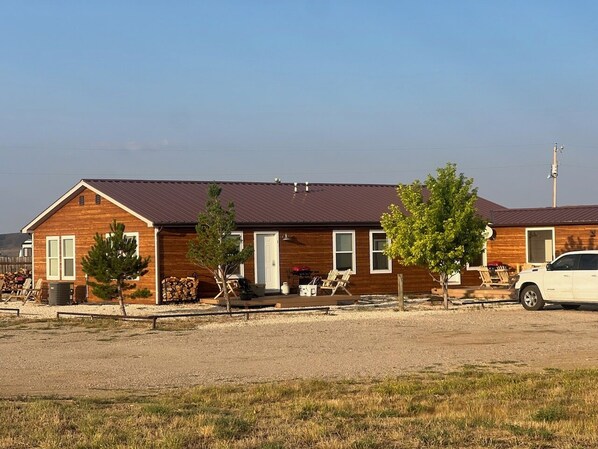 A two-story wooden cabin with a metal roof, a front porch with chairs, and a parked car.