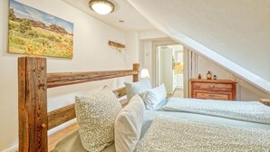 Ein Schlafzimmer mit einem hölzernen Kopfteil, einem Bett mit gemusterten Betttextilien, einem Nachttisch, einer Kommode und einem Bild an der Wand.