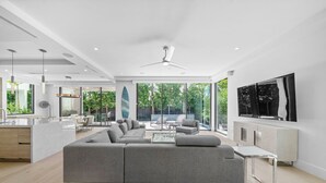 A modern living room with a large grey sectional sofa, a glass coffee table, and a dining area with a white table and chairs. - 1062 Managed by Brampton Park (Delray Beach)