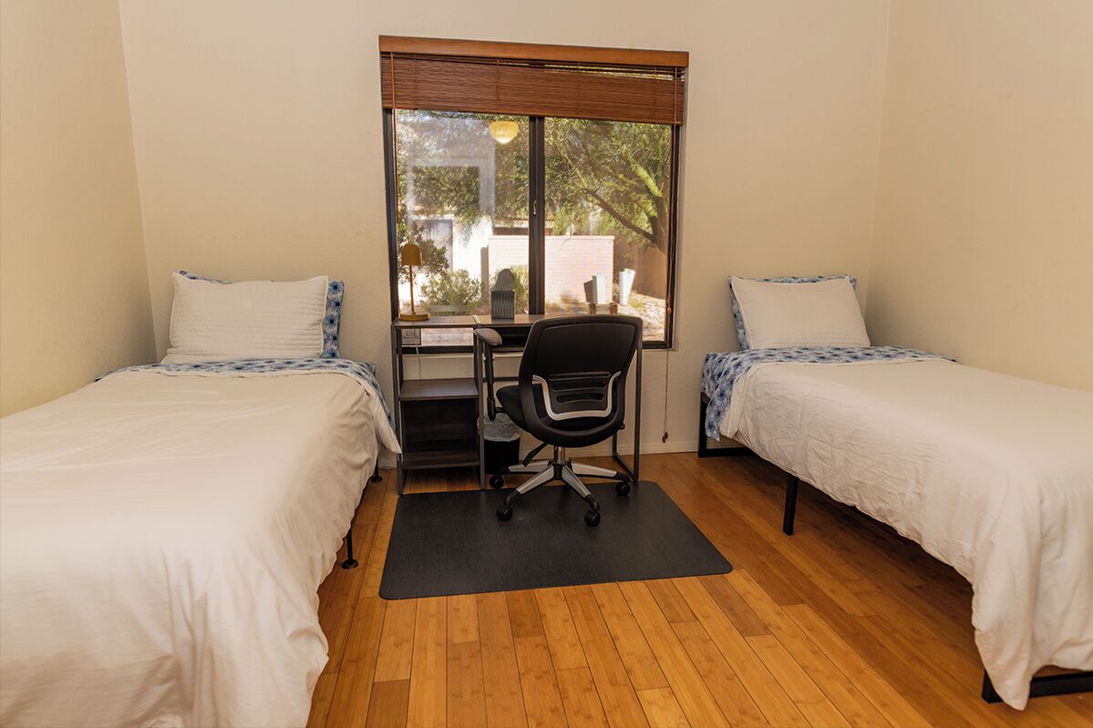 A room with two single beds, a desk, and a chair.