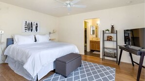 A bedroom with a bed, a gray ottoman, a ceiling fan, a TV, and a bathroom visible through an open door. - Gated Oasis:  2Bed, 2Bath, Pool & Spa, Very fast Wifi ,Garage. 2 mins from I-10. (Tucson)