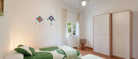 A bedroom with two beds, a wardrobe, a hanging light fixture, and a window with curtains.