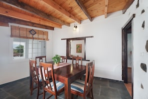 A dining area with a wooden table and chairs, a potted plant, and a window with blinds.