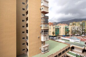 A multi-story residential building with balconies, a rooftop pool, and a view of surrounding buildings and mountains.