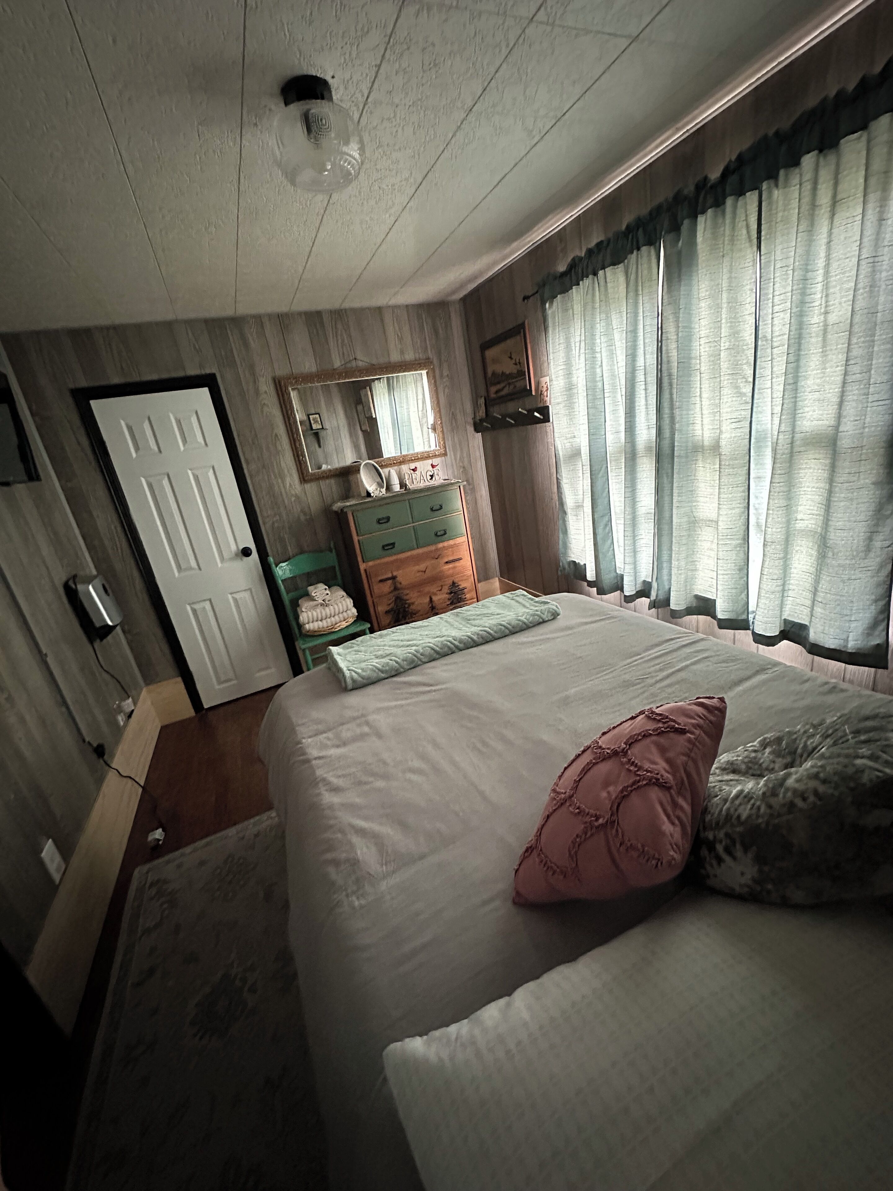 Un dormitorio con cama, cómoda, espejo y ventana con cortinas.