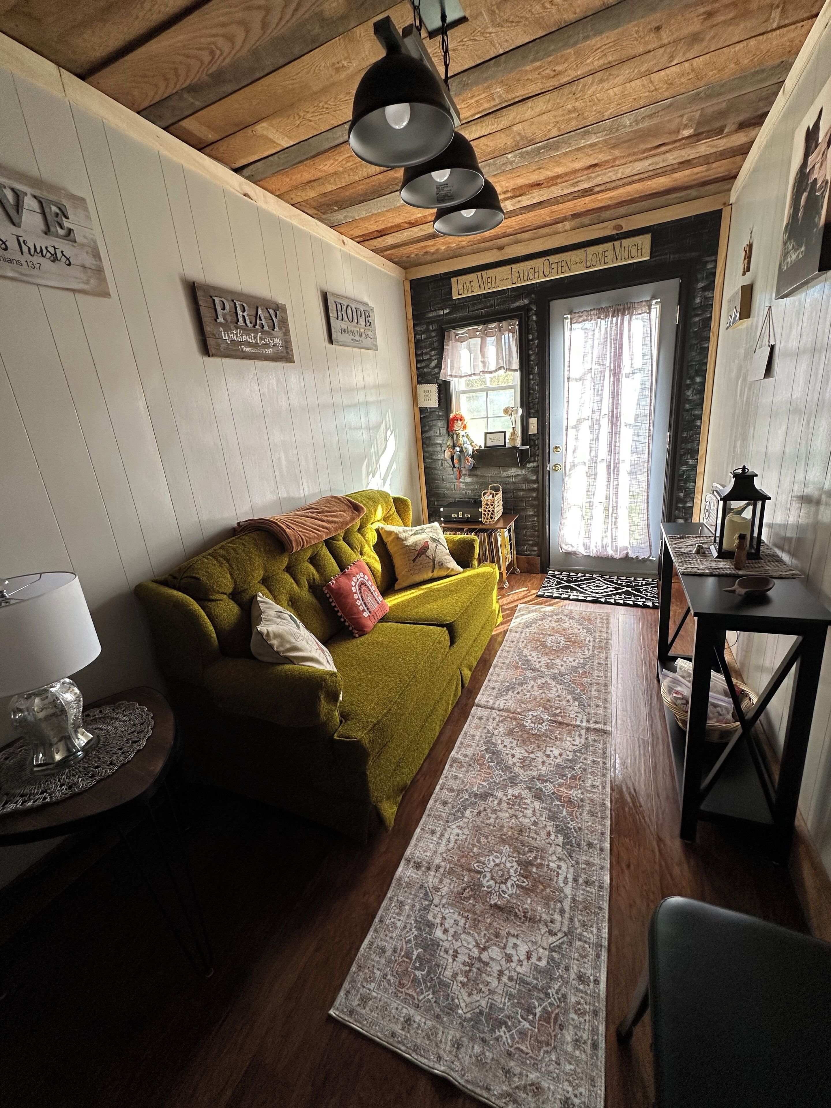 Un accogliente soggiorno con un divano verde, un tappeto decorato e un soffitto in legno.