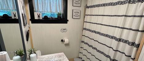 A bathroom with a sink, mirror, and a window with a view of greenery.
