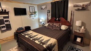 Ein Schlafzimmer mit einem großen Bett, einem Flachbildfernseher, einem Holz-Kopfteil, einem Nachttisch, einer Wandablage und einem gemusterten Teppich.