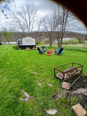 A grassy outdoor area with a small cabin, several chairs, and a fire pit. - Charming 3-bedroom house in small town of Everett PA  (Everett)