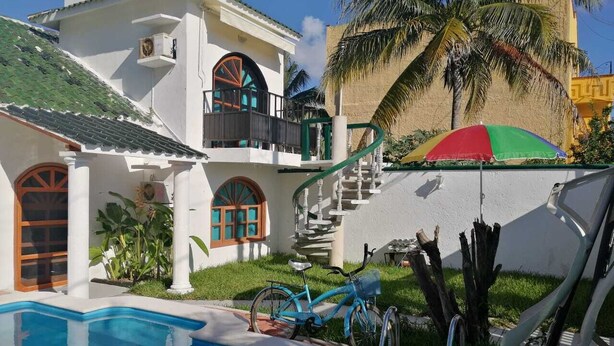 A poolside area with a blue pool, a bicycle, and a staircase leading to a balcony.