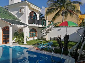 Un espace aménagé au bord d’une piscine bleue, avec un vélo et un escalier menant à un balcon.