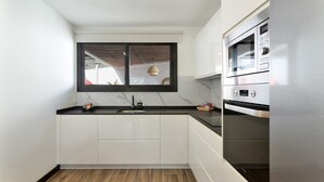Une cuisine moderne avec des meubles blancs, un plan de travail noir, une fenêtre offrant une belle vue et un four en acier inoxydable.