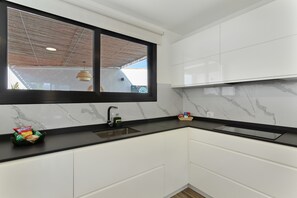 Eine moderne Küche mit weißen Schränken, einer schwarzen Arbeitsplatte, einem Fenster mit Holzbalkendecke und einem Spülbecken.