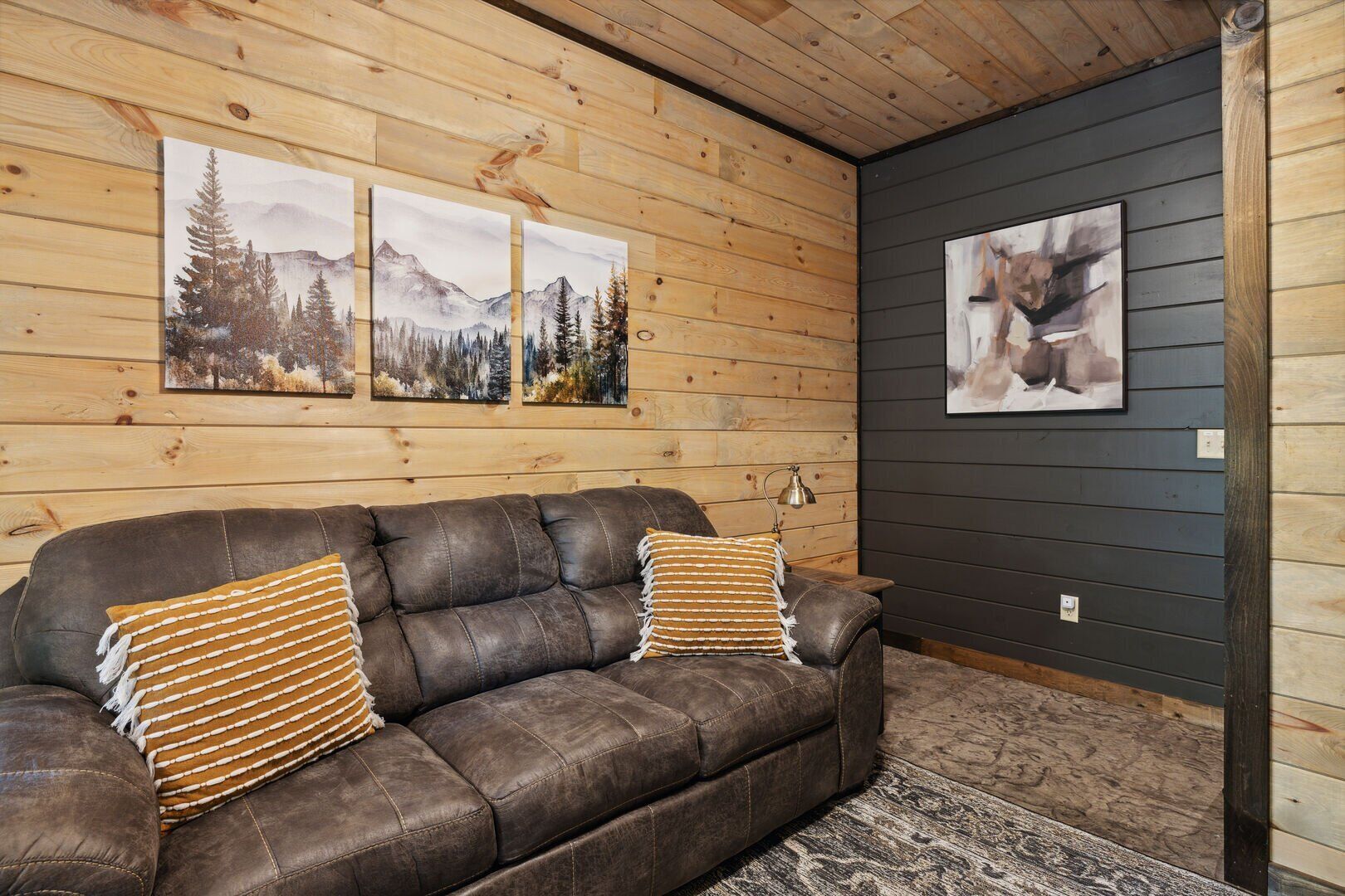 Ein gemütliches Zimmer mit einem braunen Ledersofa, zwei gestreiften Kissen und drei gerahmten Bildern an der Wand.