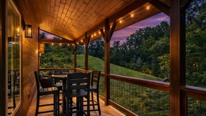 A wooden deck with a table and chairs, overlooking a lush green landscape.