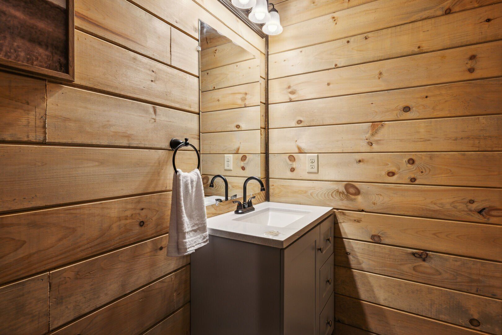 A wooden-paneled bathroom with a sink, mirror, and towel rack.