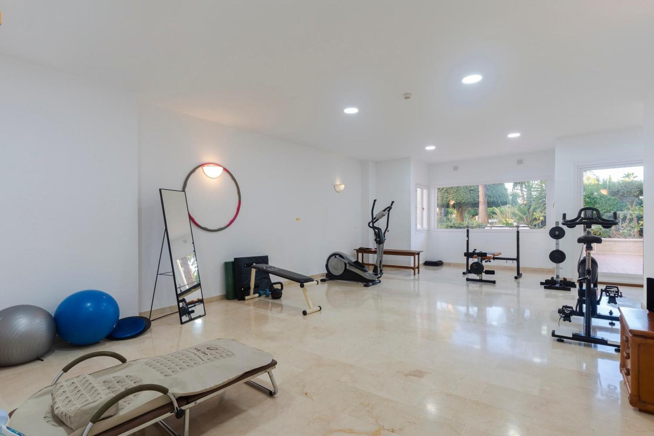 A spacious gym with various exercise equipment, a standing mirror, and a massage table.