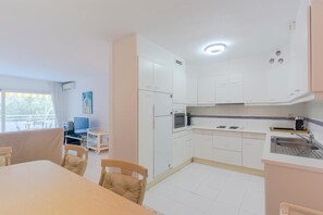 Une cuisine compacte avec des meubles blancs, un coin repas comprenant une table et des chaises, et un téléviseur placé dans un coin.