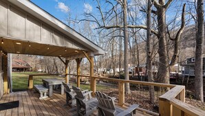 Eine Holzterrasse mit Adirondack-Stühlen und einem Tisch, mit Blick auf ein bewaldetes Gebiet.
