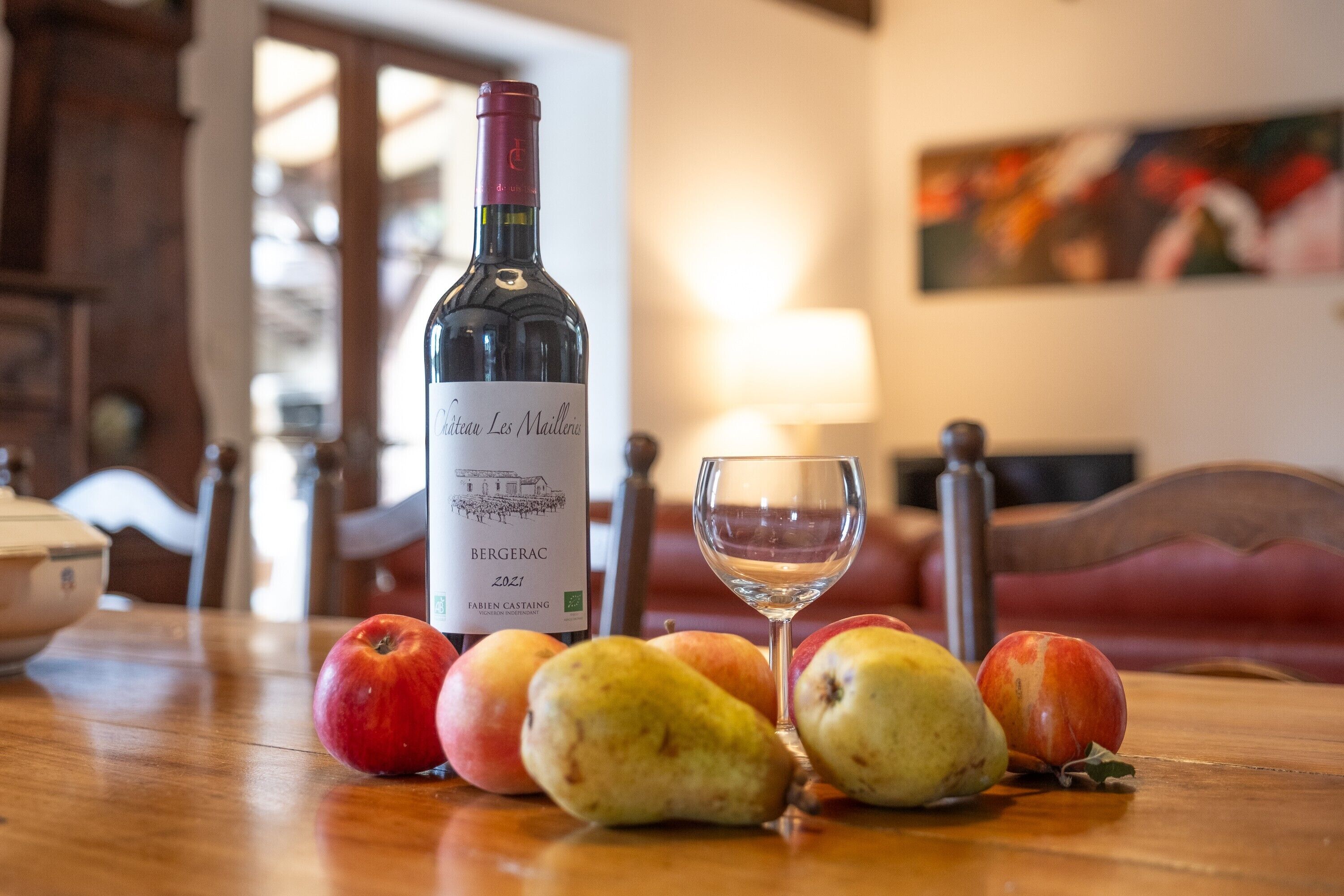 Une bouteille de vin, un verre et des fruits sur une table.