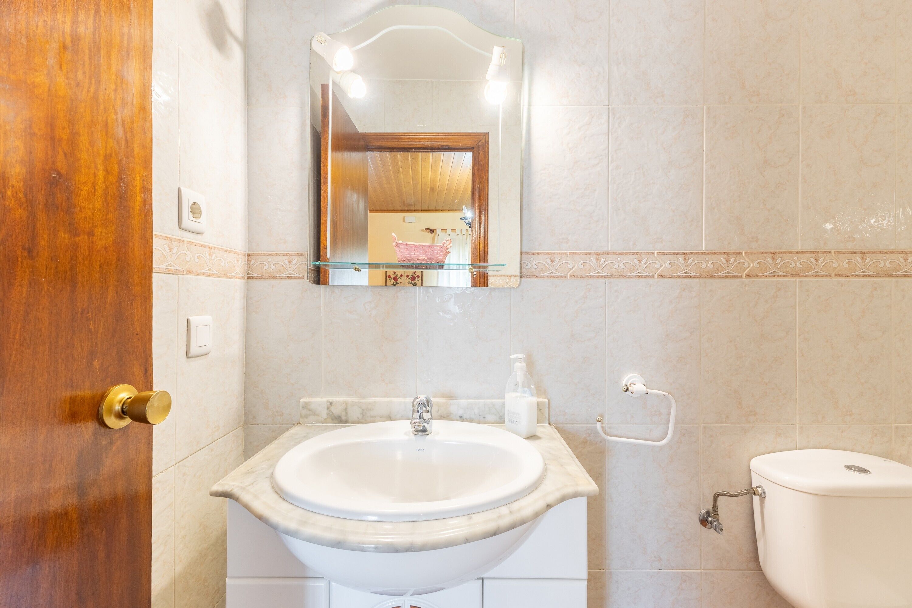 Une salle de bain avec un lavabo, un miroir, des toilettes et une porte en bois.