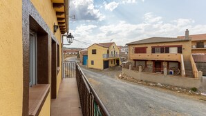 A residential street with yellow and beige houses, a paved road, and a balcony with a metal railing. - Casa Raspa Country House – Nature and Charm in Ávila (Baterna)