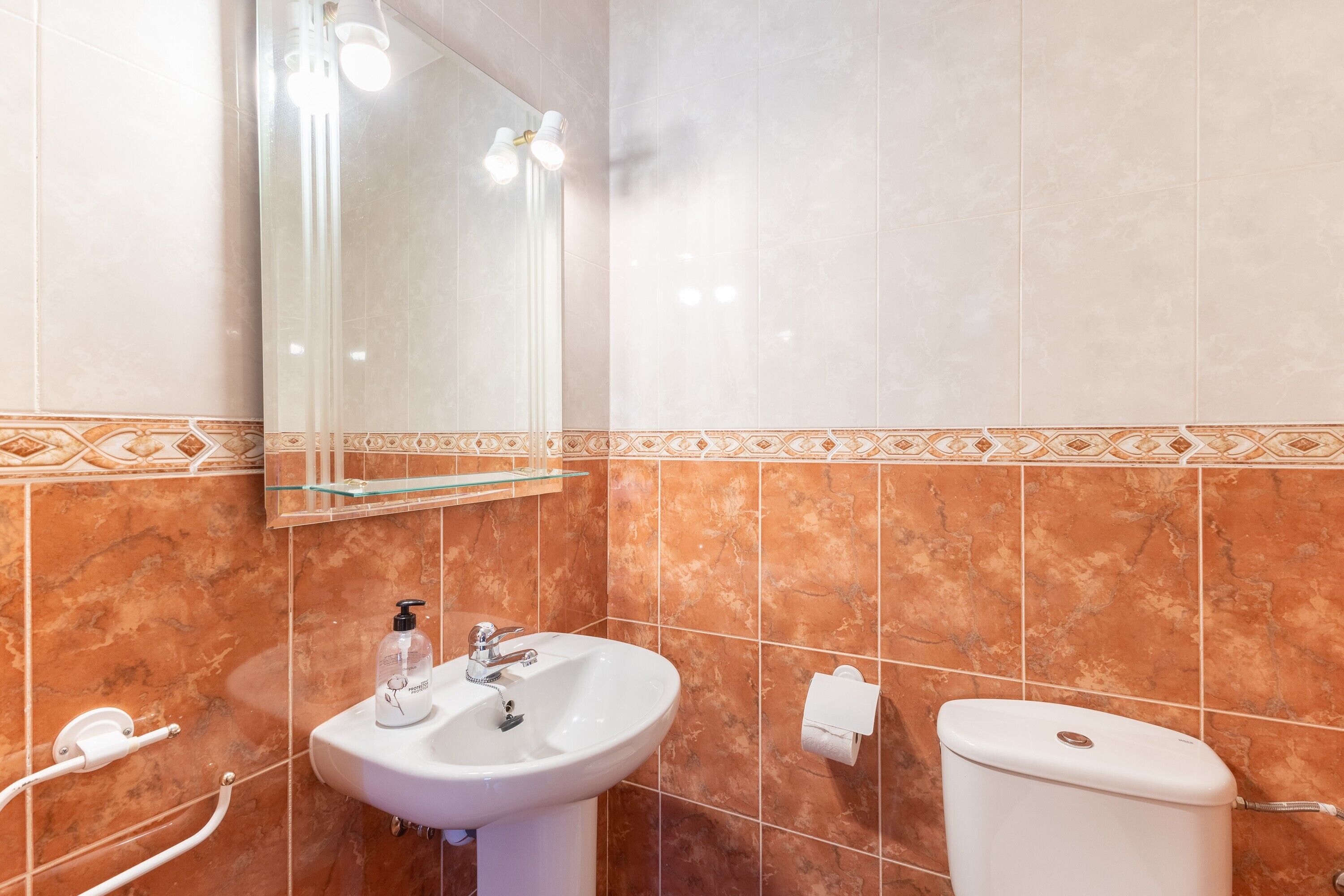 A bathroom with a sink, mirror, toilet, and decorative tile border.