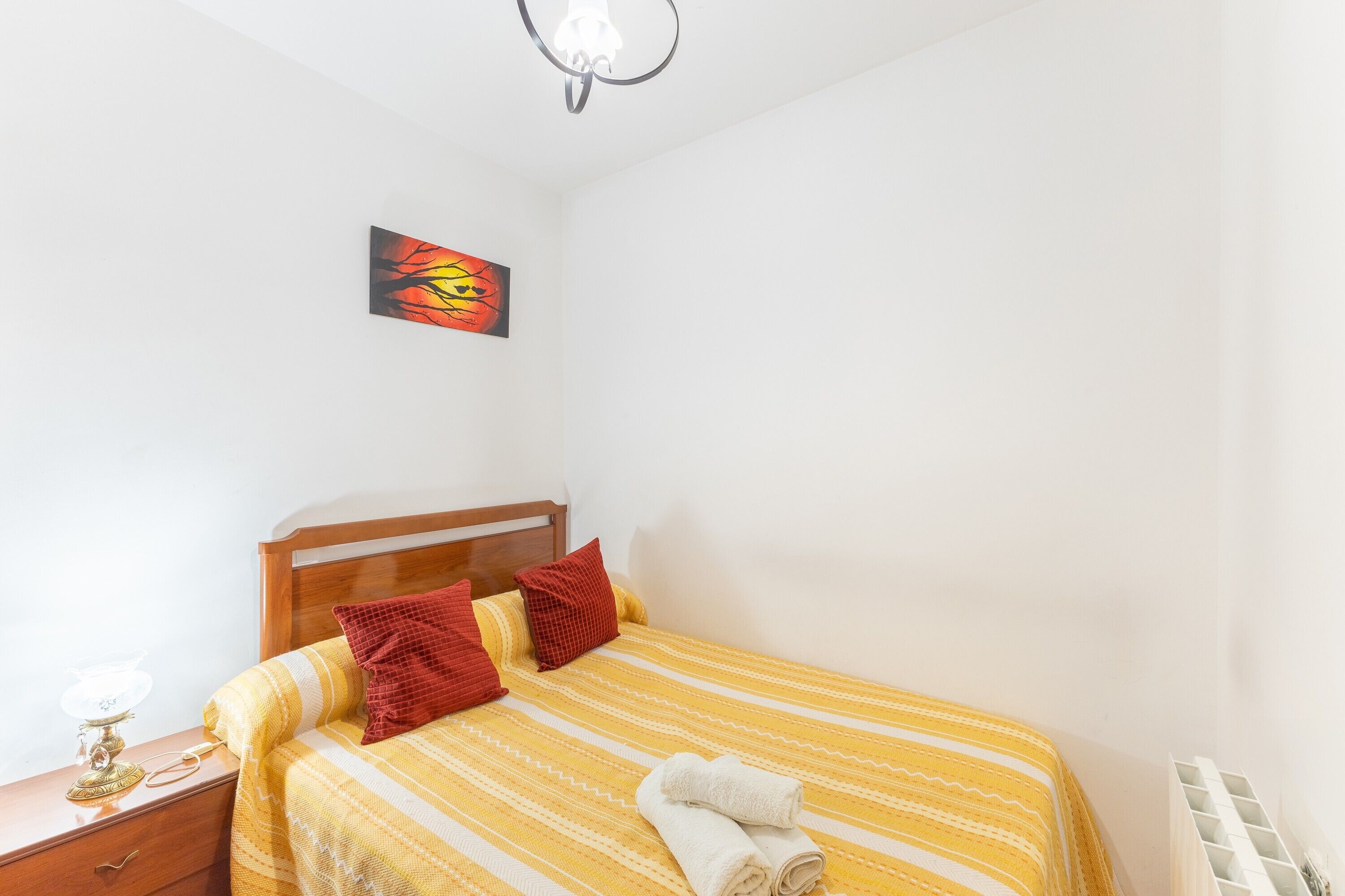 Une chambre à coucher avec un lit, une table de chevet, une lampe, un tableau et un radiateur.
