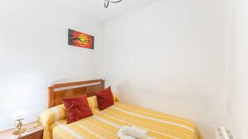 Une chambre à coucher avec un lit, une table de chevet, une lampe, un tableau et un radiateur.