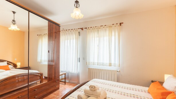 A bedroom with a bed, a wooden wardrobe, a mirror, and a window with curtains. - Casa Raspa Country House – Nature and Charm in Ávila (Baterna)