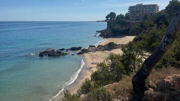 Blick auf die Küste mit Strand, felsigem Gelände und einem Gebäude im Hintergrund.