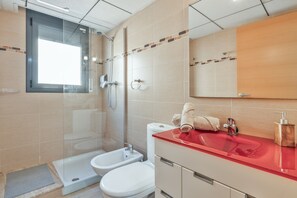 Ein Badezimmer mit einer gläsernen Duschkabine, einem Bidet, einer Toilette und einem roten Waschbecken mit Holz-Seifenspender.