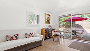 Un salon comprenant un canapé, une table, des chaises, une porte vitrée donnant sur l’extérieur et un tableau encadré accroché au mur.