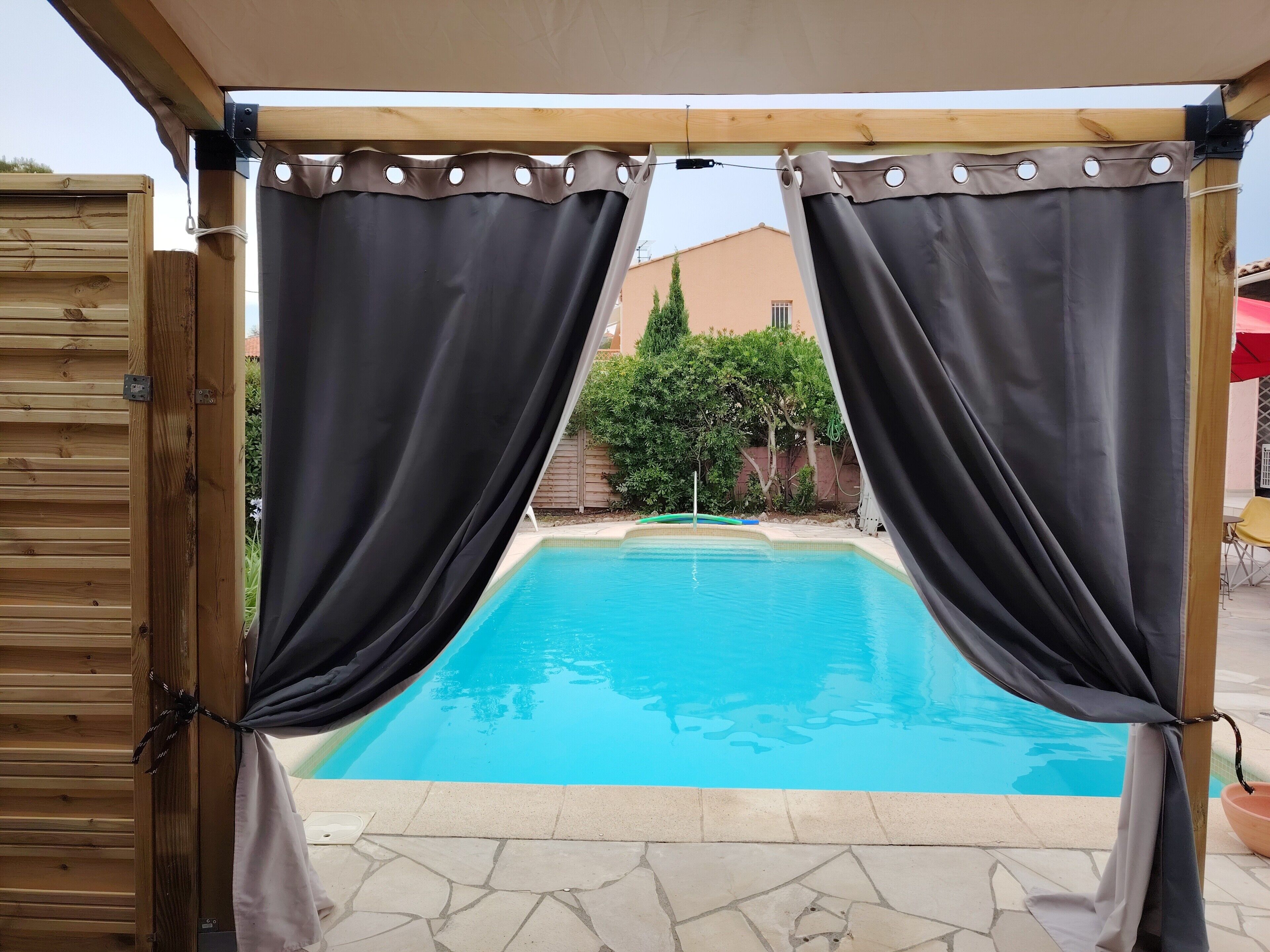 A swimming pool with a wooden deck and a covered area with curtains.
