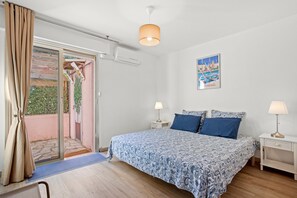 Una camera da letto con un letto, due comodini, una lampada a soffitto, una porta che dà su un balcone e un quadro appeso al muro.