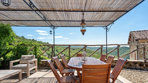 Une terrasse extérieure avec une table et des chaises en bois, une lanterne suspendue et une vue sur le paysage environnant.
