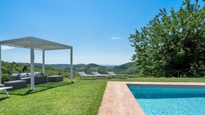 Une piscine agrémentée d’une pergola et d’un espace détente, entourée d’une pelouse verdoyante et d’arbres.