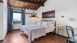 Une chambre à coucher avec un lit, une fenêtre avec des rideaux, un tableau au mur, une table de chevet et une chaise.
