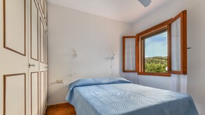 Een slaapkamer met een bed, een raam met gordijnen, een kledingkast en uitzicht op groen.