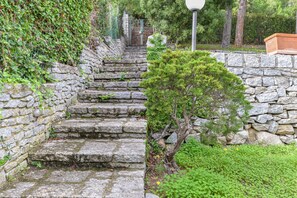 Un escalier en pierre menant à un portail, entouré de verdure et d’un lampadaire.
