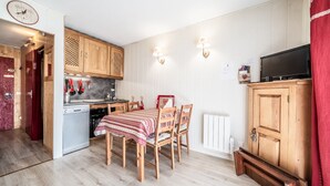 A compact kitchen with wooden cabinets, a dining table with chairs, a built-in oven, and a television on a cabinet. - Apartment 'Les Pralyssimes 462' with Mountain View, Private Terrace and Wi-Fi (Taninges)